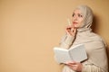Young beautiful muslim woman in hijab looking to the side with a pensive look holding a white notepad and a pencil at her chin Royalty Free Stock Photo