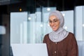 Young beautiful muslim woman in hijab working inside modern office, businesswoman using laptop at work, typing on Royalty Free Stock Photo