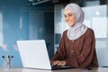 Young beautiful muslim woman in hijab working inside modern office, businesswoman using laptop at work, typing on Royalty Free Stock Photo