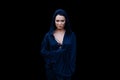 Young beautiful woman with a black hair and in the dark blue cloak with hood at the black background