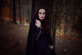 Young beautiful and mysterious woman in woods, in black cloak with hood, image of forest elf or witch