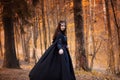 Young beautiful and mysterious woman in woods, in black cloak with hood, image of forest elf or witch Royalty Free Stock Photo