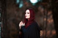 Young beautiful and mysterious woman in woods, in black cloak with hood, image of forest elf or witch Royalty Free Stock Photo