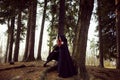 Young beautiful and mysterious woman in woods, in black cloak with hood, image of forest elf or witch Royalty Free Stock Photo