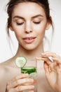 Young beautiful naked girl with perfect clean skin smiling holding glass of water with cucumber slices over white Royalty Free Stock Photo