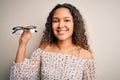 Young beautiful optical woman with curly hair holding vision glasses over white background with a happy face standing and smiling Royalty Free Stock Photo