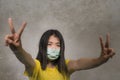 Young beautiful pacifist Asian Korean woman in face mask doing peace fingers symbol standing for human rights respect and freedom