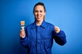 Young beautiful painter woman with blue eyes painting wearing uniform using paint brush annoyed and frustrated shouting with Royalty Free Stock Photo