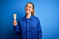 Young beautiful painter woman with blue eyes painting wearing uniform using paint brush with a happy face standing and smiling Royalty Free Stock Photo