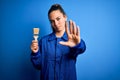 Young beautiful painter woman with blue eyes painting wearing uniform using paint brush with open hand doing stop sign with Royalty Free Stock Photo