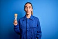 Young beautiful painter woman with blue eyes painting wearing uniform using paint brush scared in shock with a surprise face, Royalty Free Stock Photo
