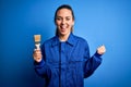 Young beautiful painter woman with blue eyes painting wearing uniform using paint brush screaming proud and celebrating victory Royalty Free Stock Photo