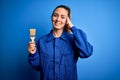 Young beautiful painter woman with blue eyes painting wearing uniform using paint brush stressed with hand on head, shocked with Royalty Free Stock Photo