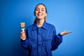 Young beautiful painter woman with blue eyes painting wearing uniform using paint brush very happy and excited, winner expression Royalty Free Stock Photo