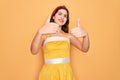 Young beautiful pin up woman wearing 50s fashion vintage dress over yellow background approving doing positive gesture with hand, Royalty Free Stock Photo