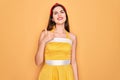 Young beautiful pin up woman wearing 50s fashion vintage dress over yellow background doing happy thumbs up gesture with hand Royalty Free Stock Photo