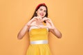 Young beautiful pin up woman wearing 50s fashion vintage dress over yellow background smiling in love doing heart symbol shape Royalty Free Stock Photo