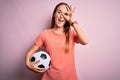 Young beautiful player woman playing soccer holding football ball  over pink background with happy face smiling doing ok sign with Royalty Free Stock Photo