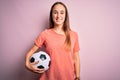 Young beautiful player woman playing soccer holding football ball  over pink background with a happy face standing and smiling Royalty Free Stock Photo