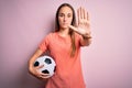 Young beautiful player woman playing soccer holding football ball  over pink background with open hand doing stop sign with Royalty Free Stock Photo