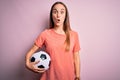 Young beautiful player woman playing soccer holding football ball  over pink background scared in shock with a surprise face, Royalty Free Stock Photo