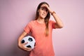 Young beautiful player woman playing soccer holding football ball  over pink background stressed with hand on head, shocked with Royalty Free Stock Photo