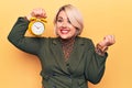 Young beautiful plus size blonde woman holding vintage alarm clock over yellow background screaming proud, celebrating victory and Royalty Free Stock Photo