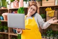 Young beautiful plus size woman florist talking on smartphone using laptop at flower shop Royalty Free Stock Photo