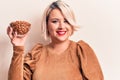 Young beautiful plus size woman holding bowl with healthy almonds over white background looking positive and happy standing and Royalty Free Stock Photo