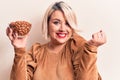 Young beautiful plus size woman holding bowl with healthy almonds over white background screaming proud, celebrating victory and Royalty Free Stock Photo