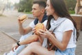 Young beautiful positive couple eating hambergers sitting on beach Royalty Free Stock Photo