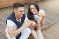 Young beautiful positive couple eating hambergers sitting on beach Royalty Free Stock Photo