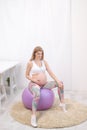 A young beautiful pregnant Caucasian woman sits on the soft carpet of the house. He is engaged in fitness and doing Royalty Free Stock Photo