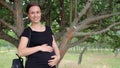 A young, beautiful, pregnant girl, near a tree, in a black T-shirt.