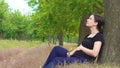 A young, beautiful, pregnant girl sits under a tree in a black T-shirt