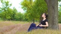 A young, beautiful, pregnant girl sits under a tree in a black T-shirt