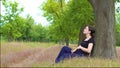 A young, beautiful, pregnant girl sits under a tree in a black T-shirt