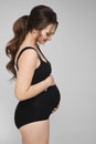 Portrait of a young beautiful pregnant woman in black bodysuit posing over gray background, isolated, copy space on the Royalty Free Stock Photo