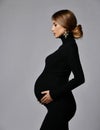 Young beautiful pregnant woman in black dress and massive cross earrings standing and looking down Royalty Free Stock Photo