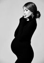 Young beautiful pregnant woman in black dress and massive earrings standing and looking down Royalty Free Stock Photo