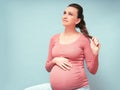 Young beautiful pregnant woman dreams over isolated blue background.