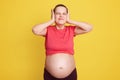 Young beautiful pregnant woman expecting baby, covering ears with palms, posing with annoyed expression for noise of loud music,