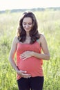 Young beautiful pregnant woman holding tummy smiling, in red a light summer dress, happy on meadow the grass Royalty Free Stock Photo