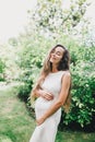 Young beautiful pregnant woman with long healthy curly hair posing in a green park. Royalty Free Stock Photo