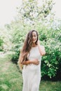 Young beautiful pregnant woman with long healthy curly hair posing in a green park. Royalty Free Stock Photo