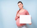 Young beautiful pregnant woman over isolated blue background holding a blank sheet of paper Royalty Free Stock Photo