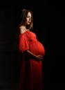 Young beautiful pregnant woman in red dress standing, embracing belly and smiling Royalty Free Stock Photo