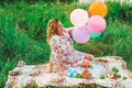 Young beautiful pregnant woman sitting at a picnic on a blanket in the park with colorful balloons in hands closeup Royalty Free Stock Photo