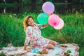 Young beautiful pregnant woman sitting at a picnic on a blanket in the park with colorful balloons in hands closeup Royalty Free Stock Photo