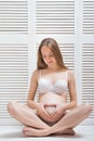 Young beautiful pregnant woman sitting in pose of Lotus and put hands in heart shape on stomach. Vertical frame Royalty Free Stock Photo